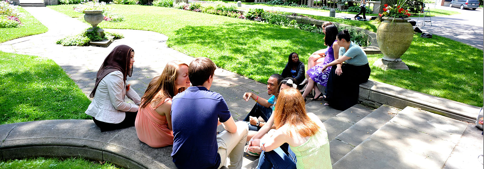 Diverse group of post secondary school students sitting on steps outside school in the sunshine