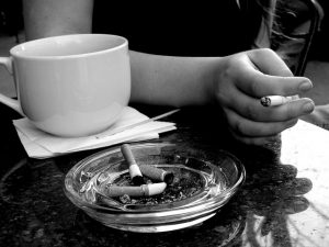 Picture of a hand holding a cigarette next to a cup of coffee.